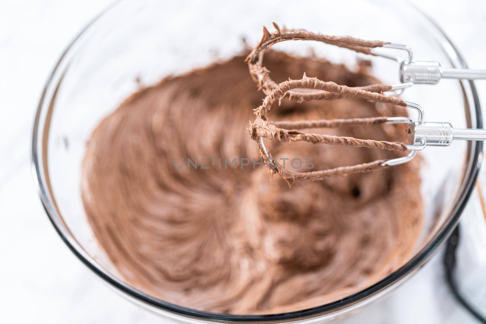 Mixing store-bought chocolate frosting in a mixing glass bowl with a hand mixer.