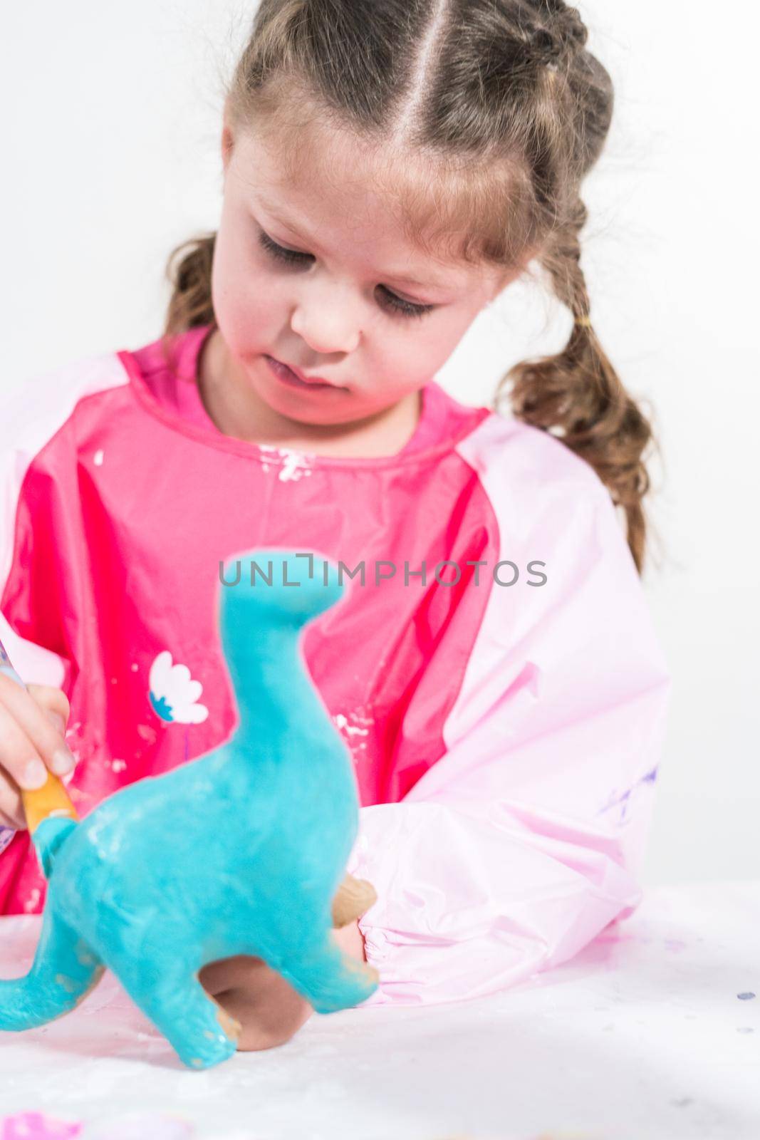 Homeschooling during COVID-19 lockdown. Little girl painting paper mache dinosaur figurine with acrylic paint.