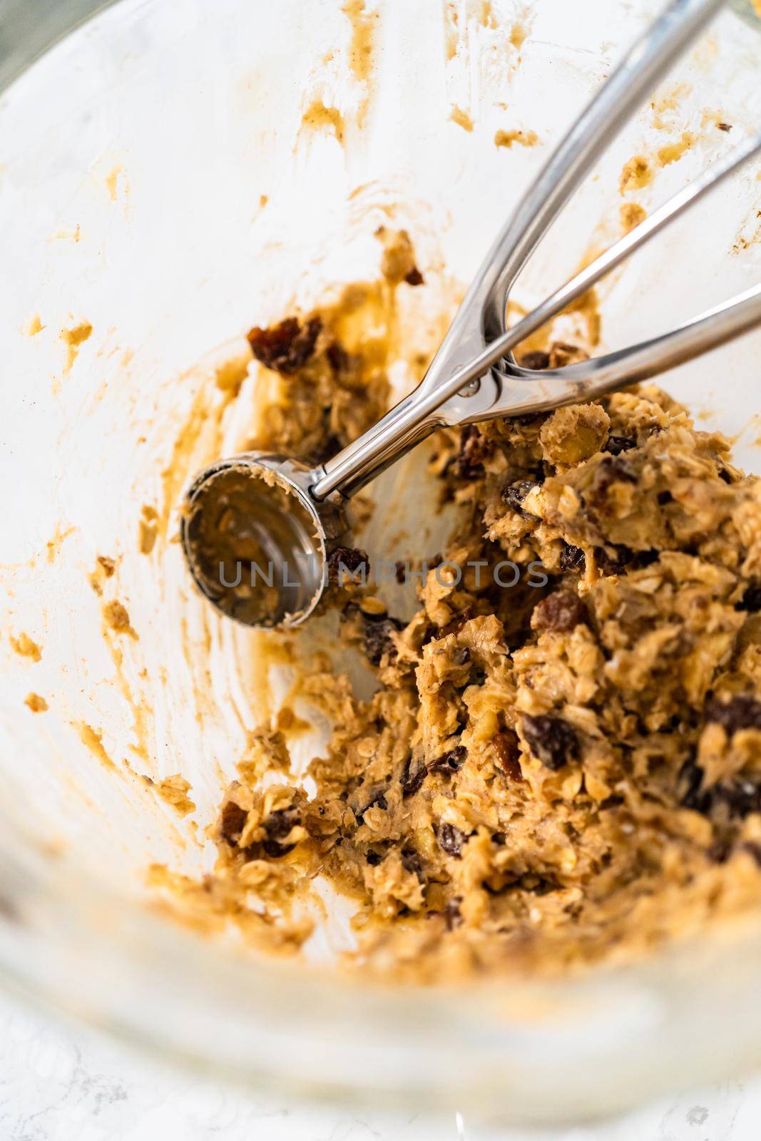 Scooping cookie dough with dough scoop into a baking sheet lined with parchment paper to bake soft oatmeal raisin walnut cookies.