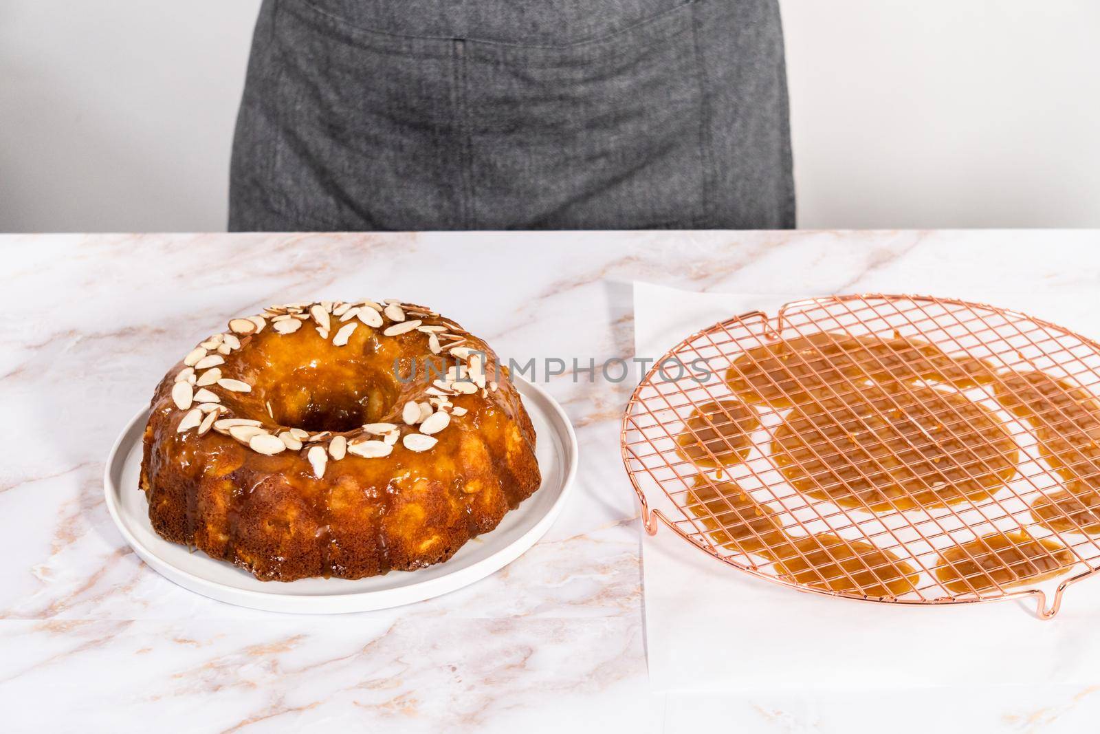Glazing homemade caramel glaze over freshly baked apple bundt cake and garnishing with sliced almonds.