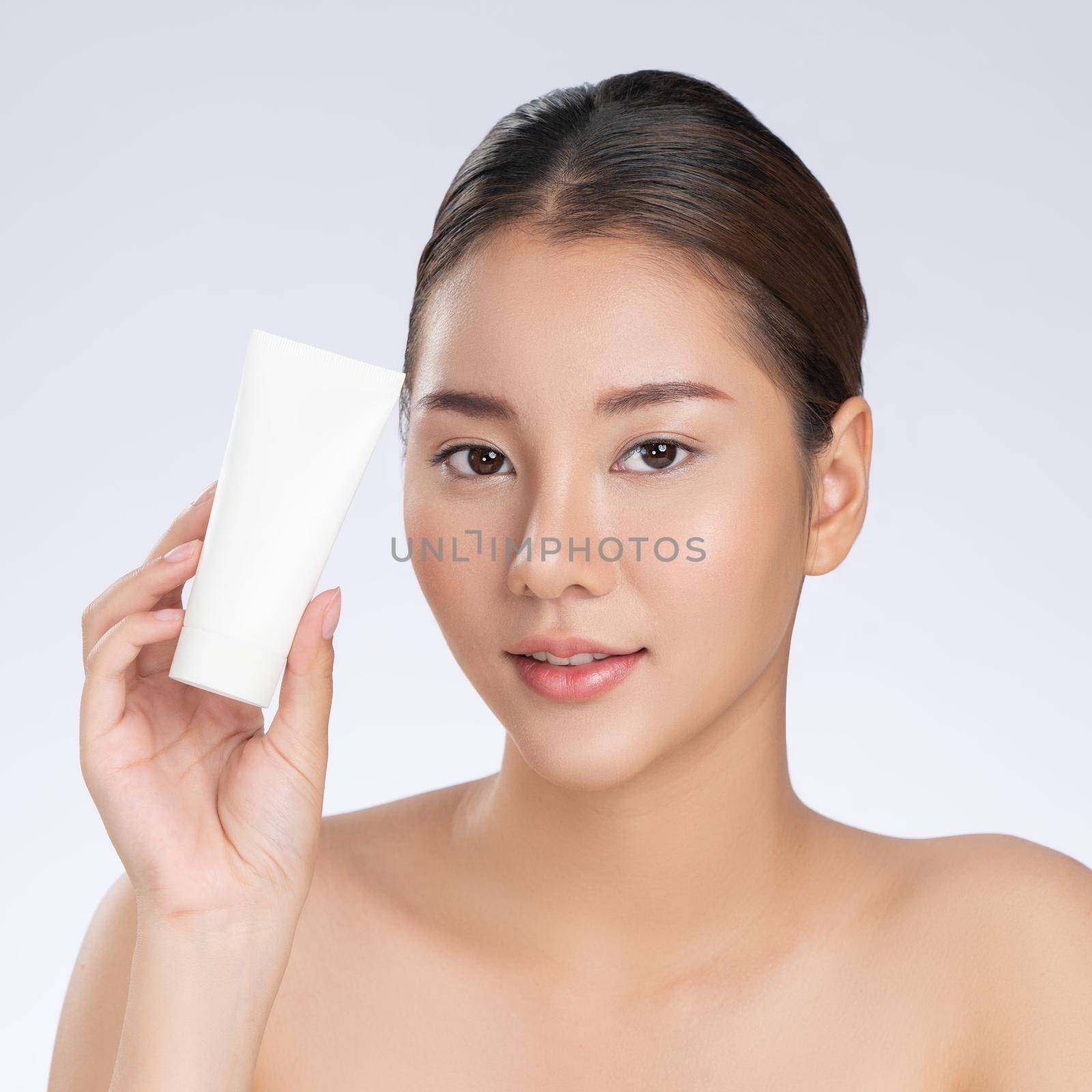 Gorgeous woman smiling holding mockup product for advertising text place, light grey background. Concept of healthcare for skin, beauty care product for advertising.
