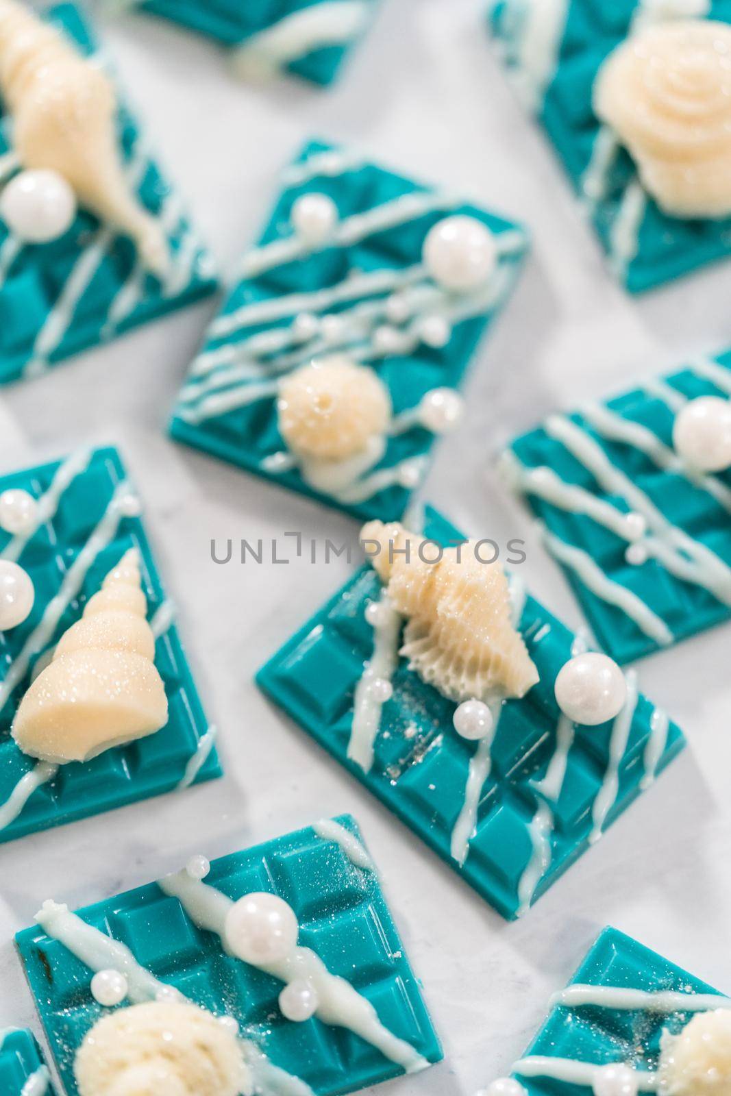 Mini mermaid chocolate bars drizzled with white chocolate, sprinkling with white pearl sugar sprinkles, and decorated with a white chocolate seashells.