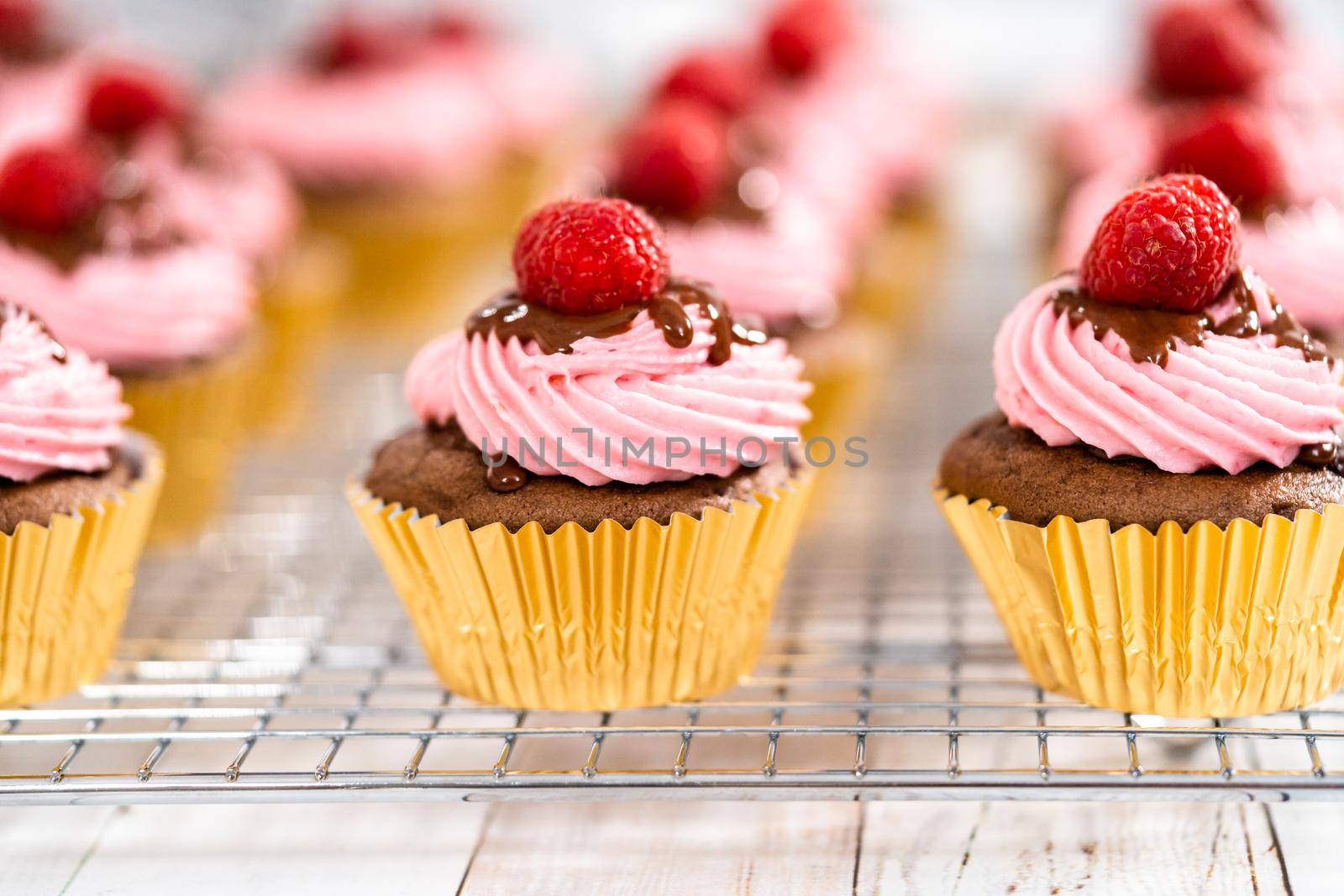 Gourmet chocolate raspberry cupcakes drizzled with chocolate ganache and topped with a fresh raspberry.