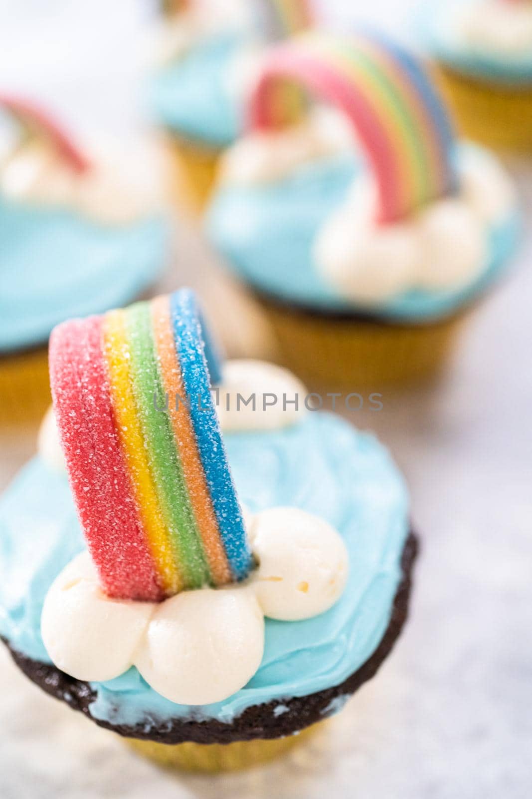 Chocolate cupcakes decorated with blue buttercream frosting and rainbow for unicorn theme birthday party.