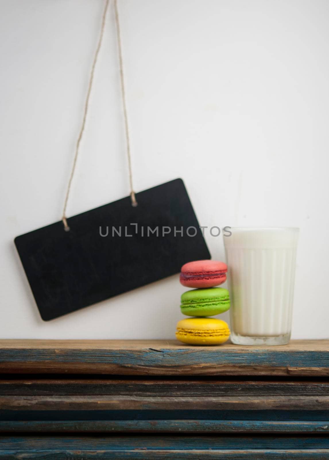 Glass of milk with colorful macaroons on wood table over white wall