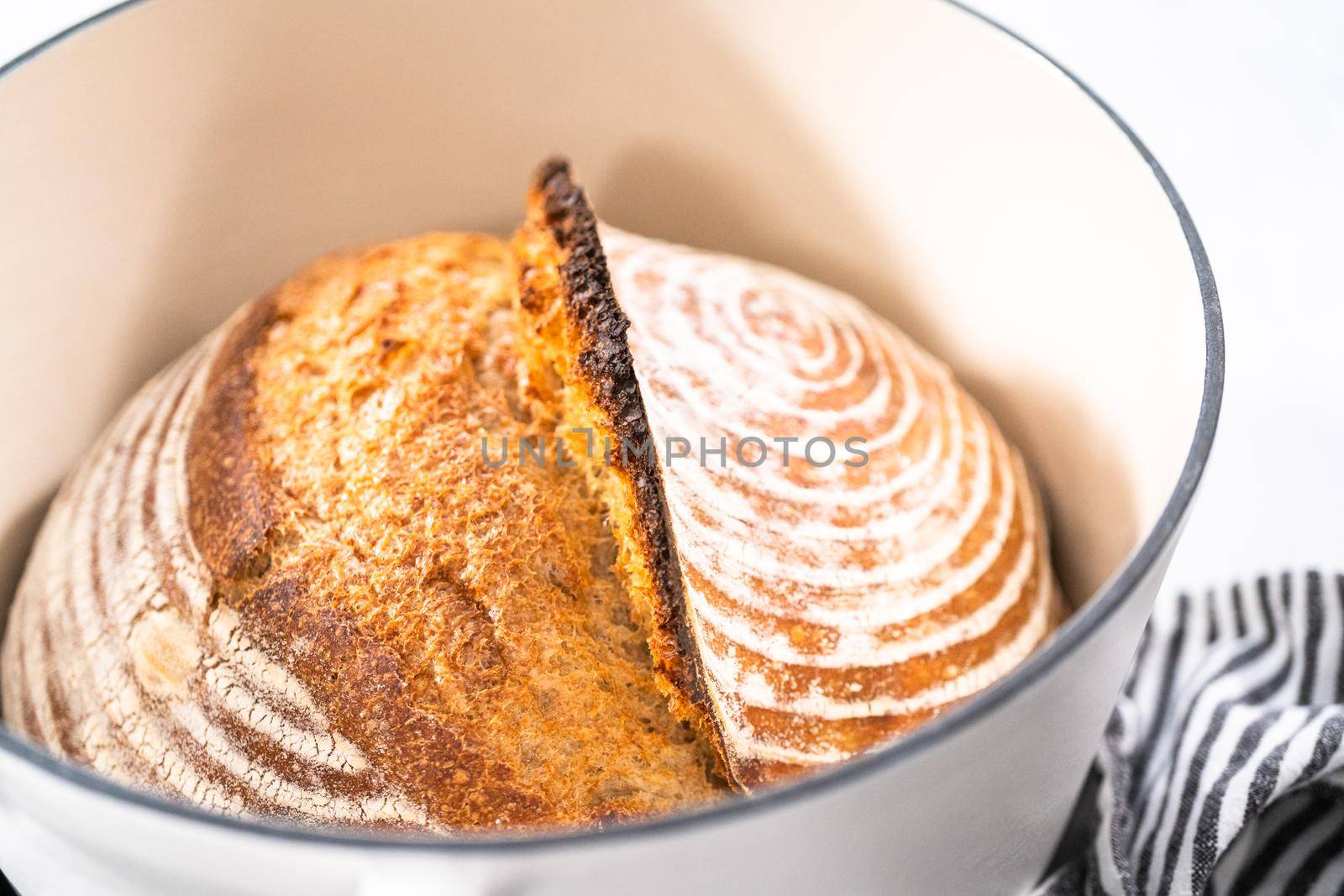 Freshly baked loaf of a wheat sourdough bread with marks from bread proofing basket in enameled cast iron dutch oven.