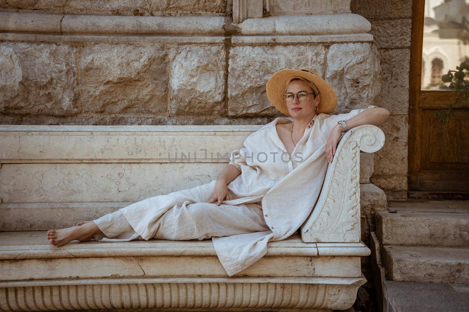 a beautiful mature woman sits on a stone bench in a hat and rests.