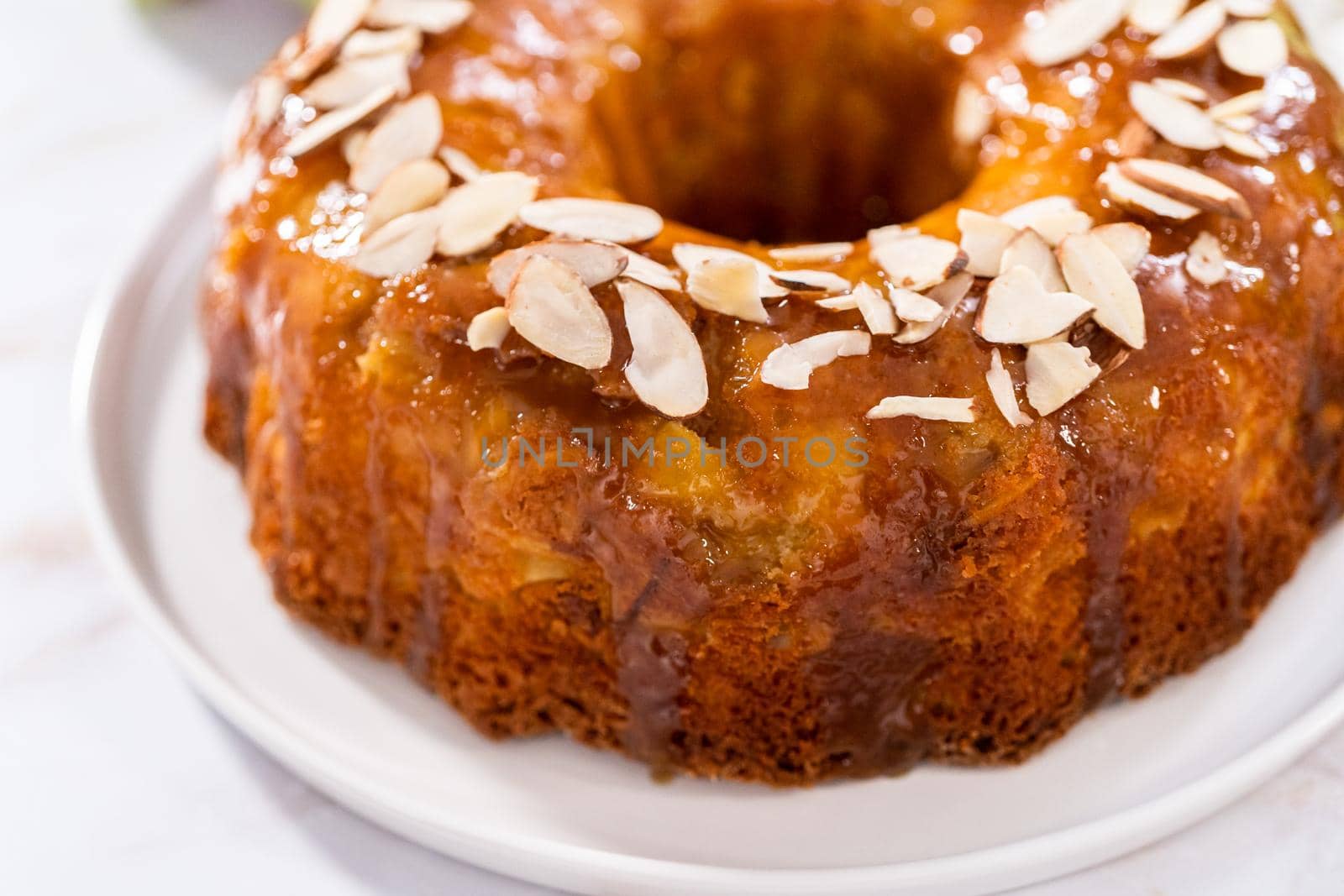 Freshly baked apple bundt cake with caramel glaze on a white plate.