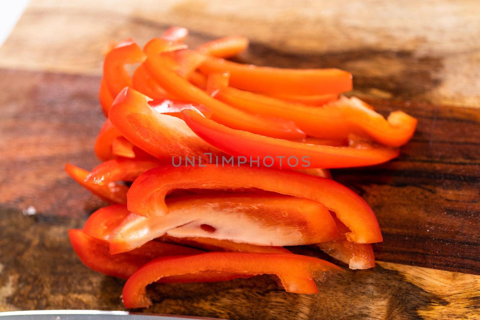 Cutting organic red bell peppers on a wood cutting board.