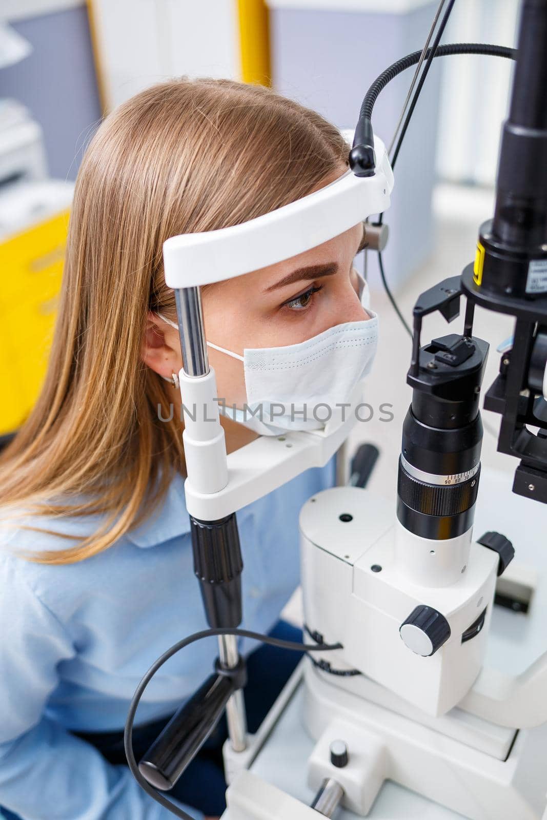 Young woman sitting in armchair looking at slit lamp during medical examination in eyes