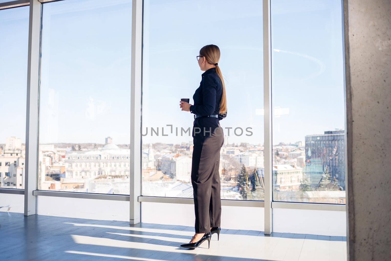 Confident business woman boss standing in modern office or hotel window enjoying big city view, woman leader, business owner thinking about future success, planning new opportunities,