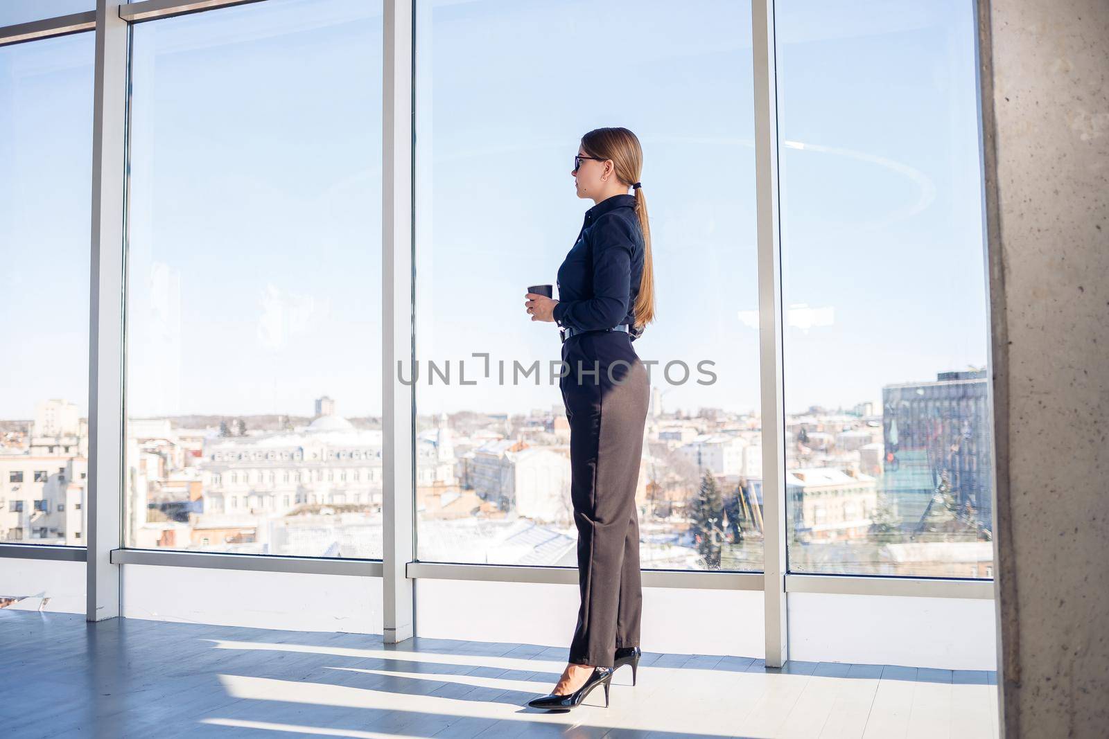 Confident business woman boss standing in modern office or hotel window enjoying big city view, woman leader, business owner thinking about future success, planning new opportunities,