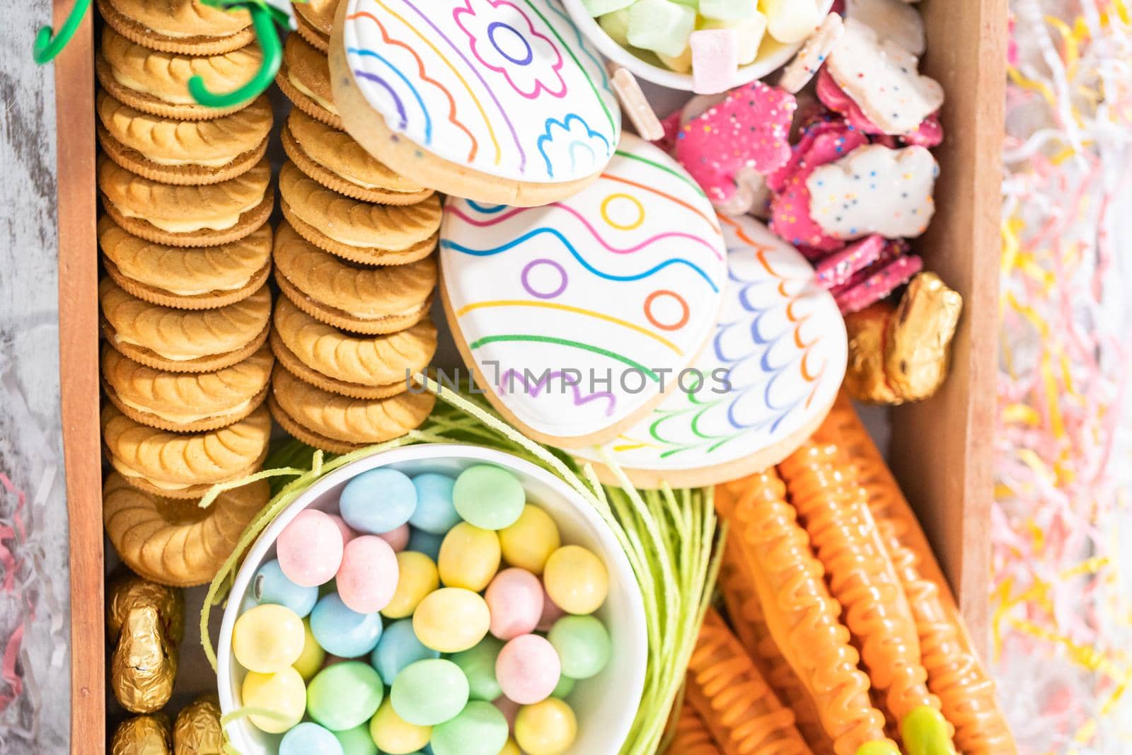 Assembling charcuterie board with Easter candies, cookies, and marshmallows.