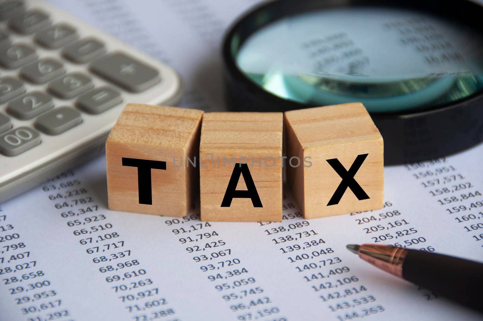 Tax word on wooden blocks with magnifying glass, calculator and number analysis background. Tax concept.