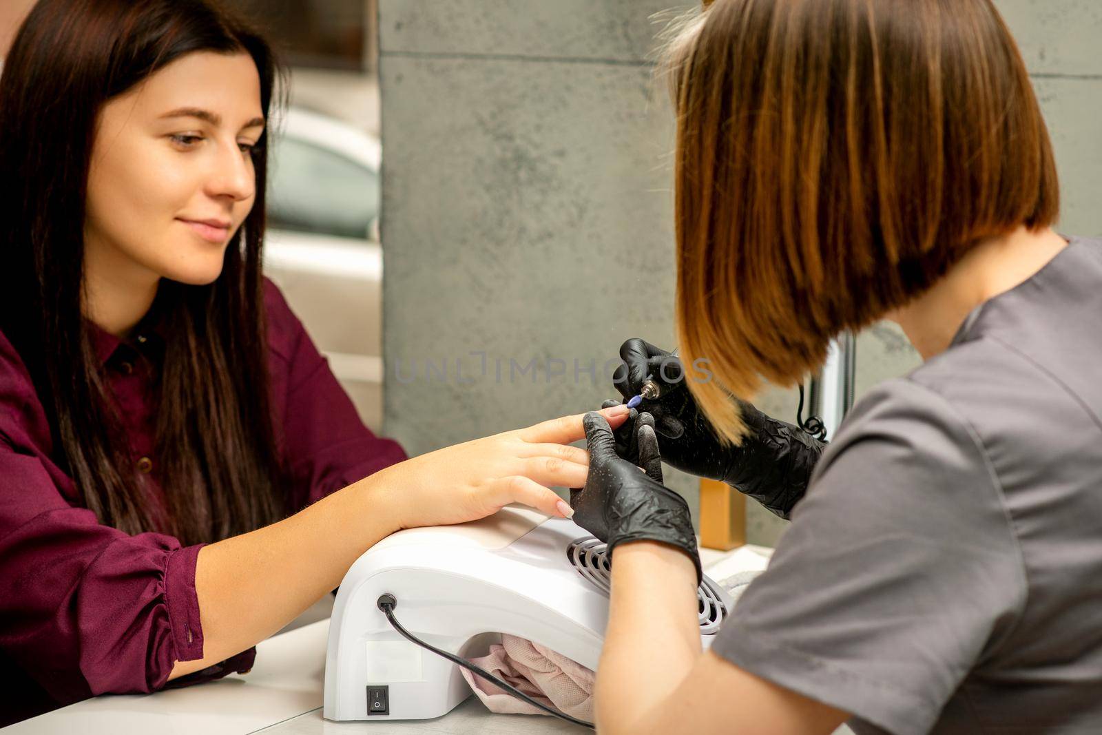 Manicure master in rubber gloves applies an electric nail file to remove the nail polish in a nail salon