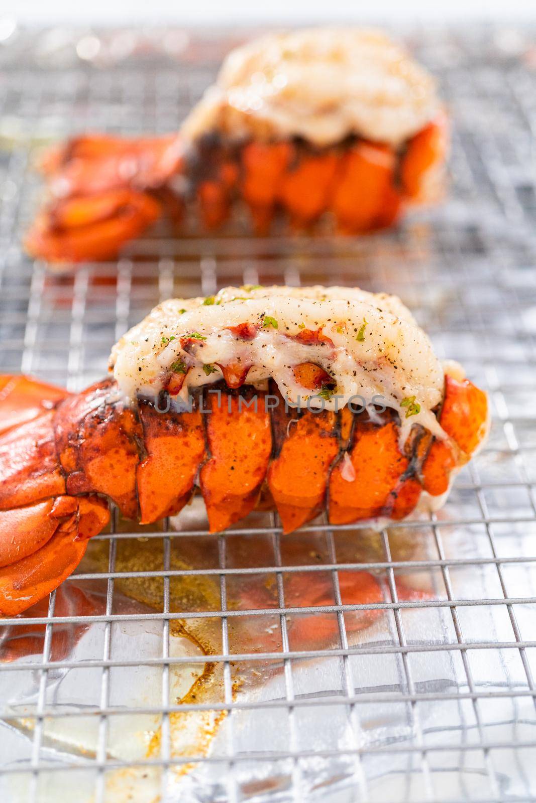 Buttering lobster tails on a baking sheet with kitchen foil.