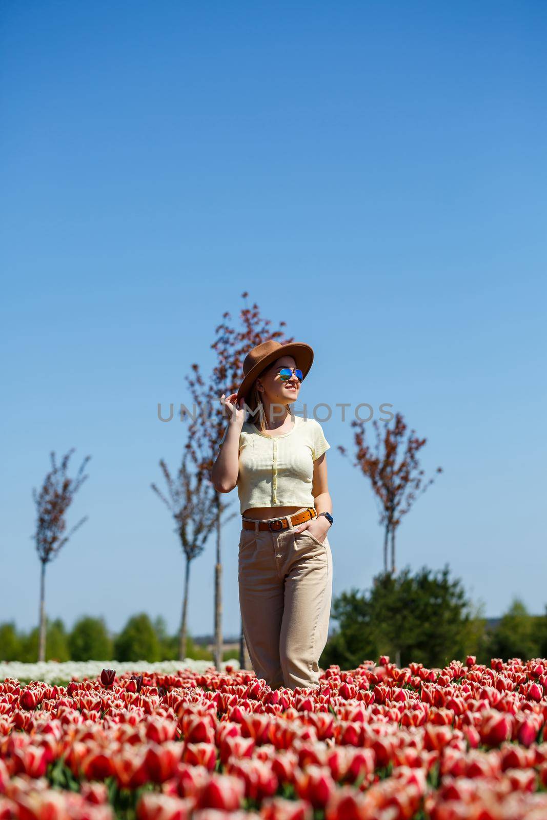 A beautiful slender woman in a hat stands in a blooming field of tulips. Spring time