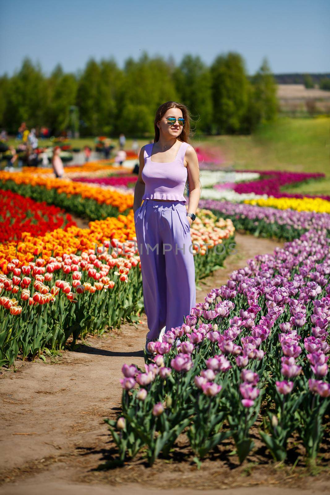 A young woman in a pink suit stands in a blooming field of tulips. Spring time