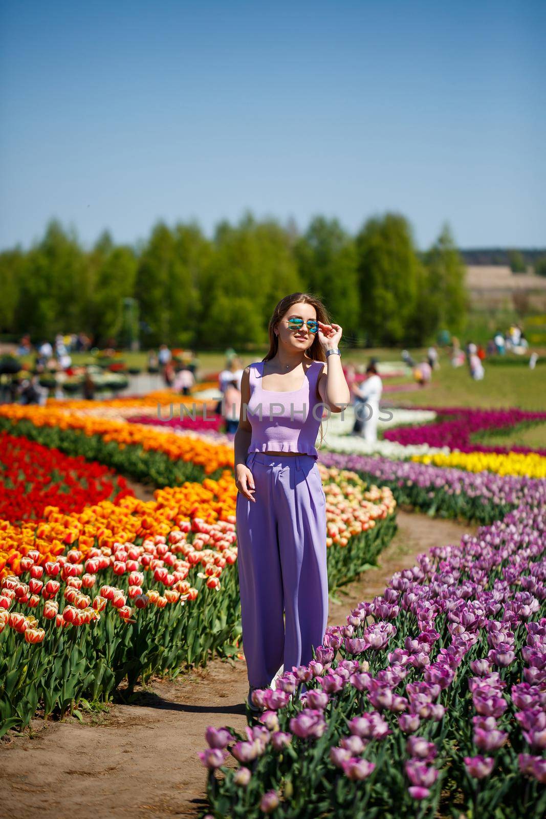 A young woman in a pink suit stands in a blooming field of tulips. Spring time