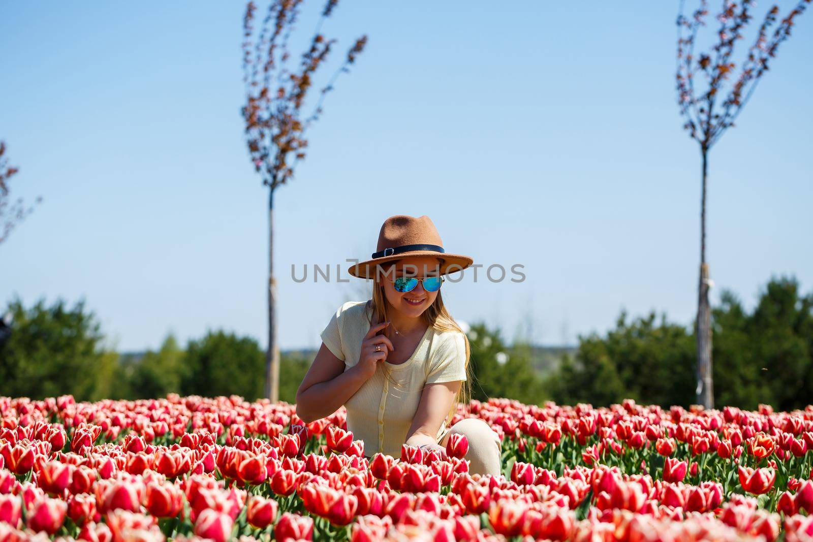 A beautiful slender woman in a hat stands in a blooming field of tulips. Spring time