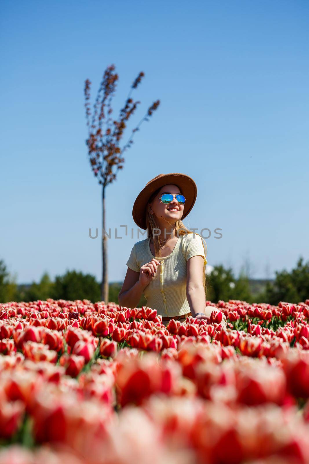 A beautiful slender woman in a hat stands in a blooming field of tulips. Spring time by Dmitrytph