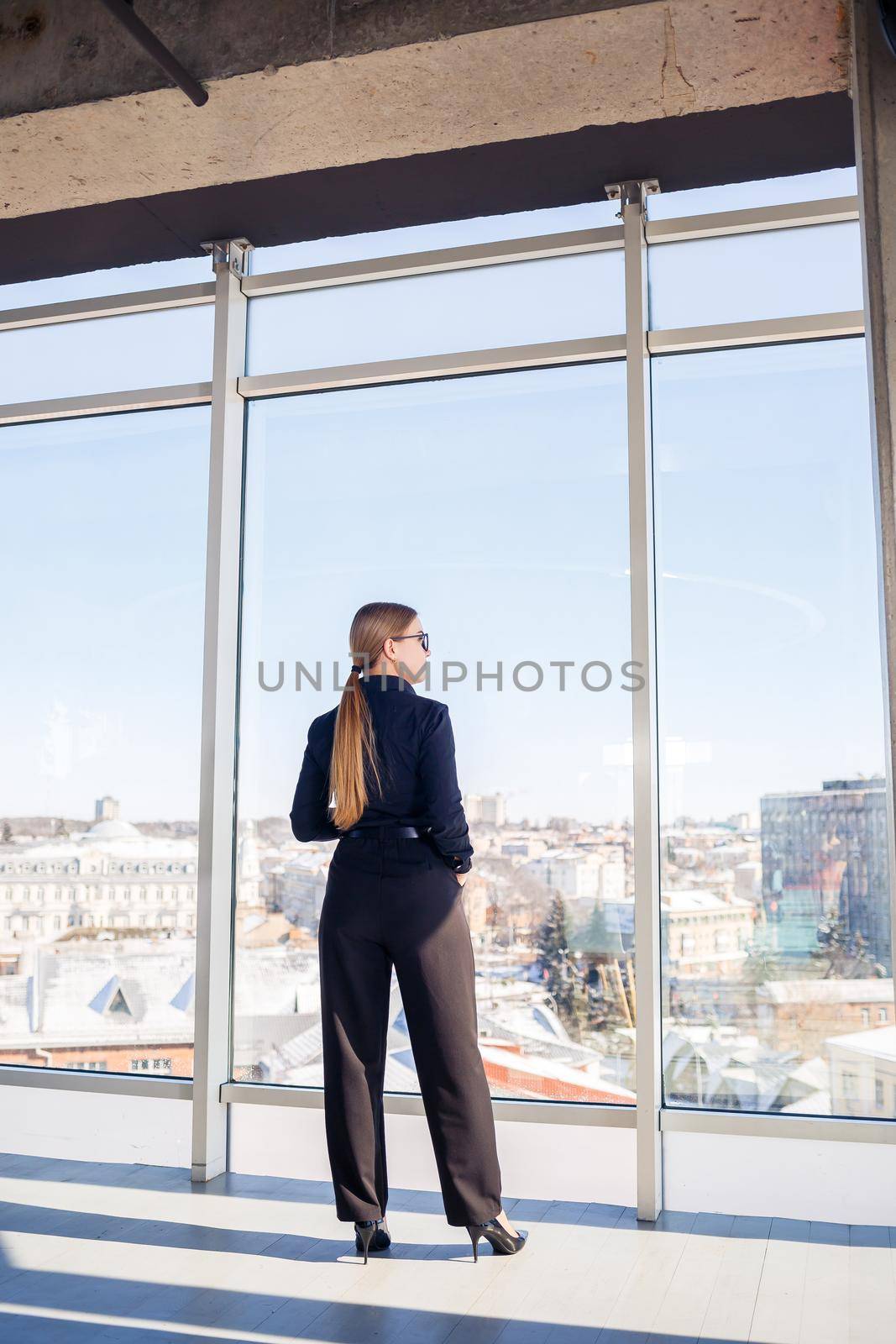 Confident business woman boss standing in modern office or hotel window enjoying big city view, woman leader, business owner thinking about future success, planning new opportunities,