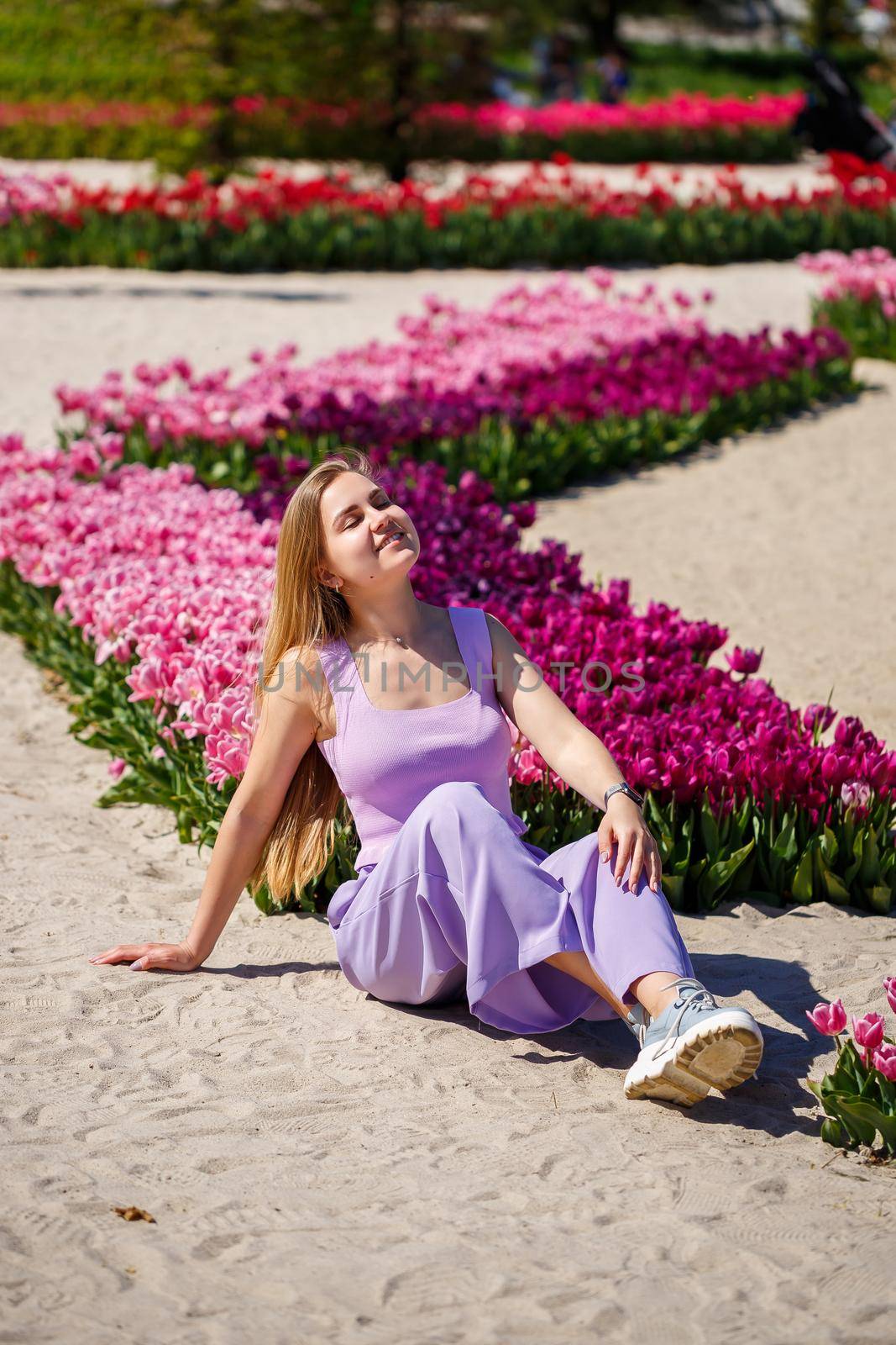 Back view of anonymous woman in summer dress and hat walking near blooming tulips in meadow on sunny day in nature by Dmitrytph