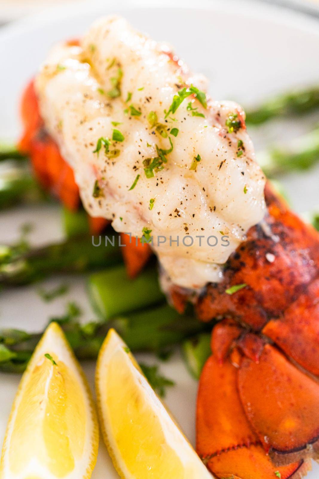 Sering garlic lobster tails with steamed asparagus and lemon wedges on a white plate.