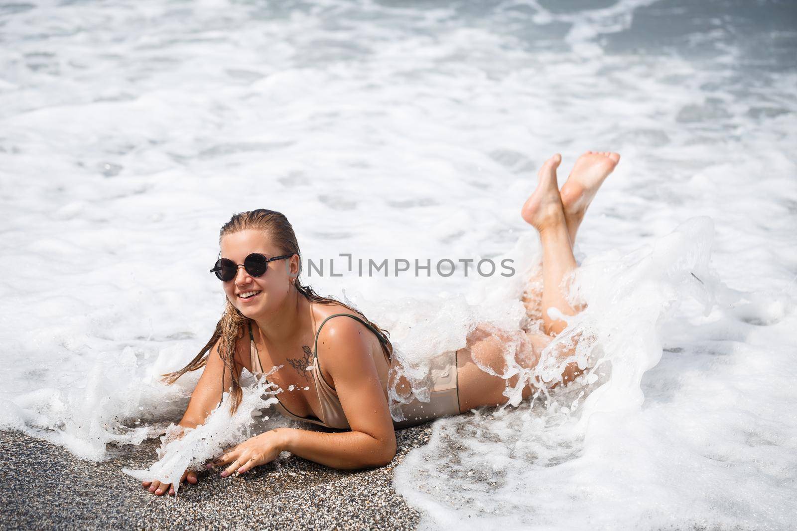 woman in beige swimsuit lies on an empty sandy beach near the ocean