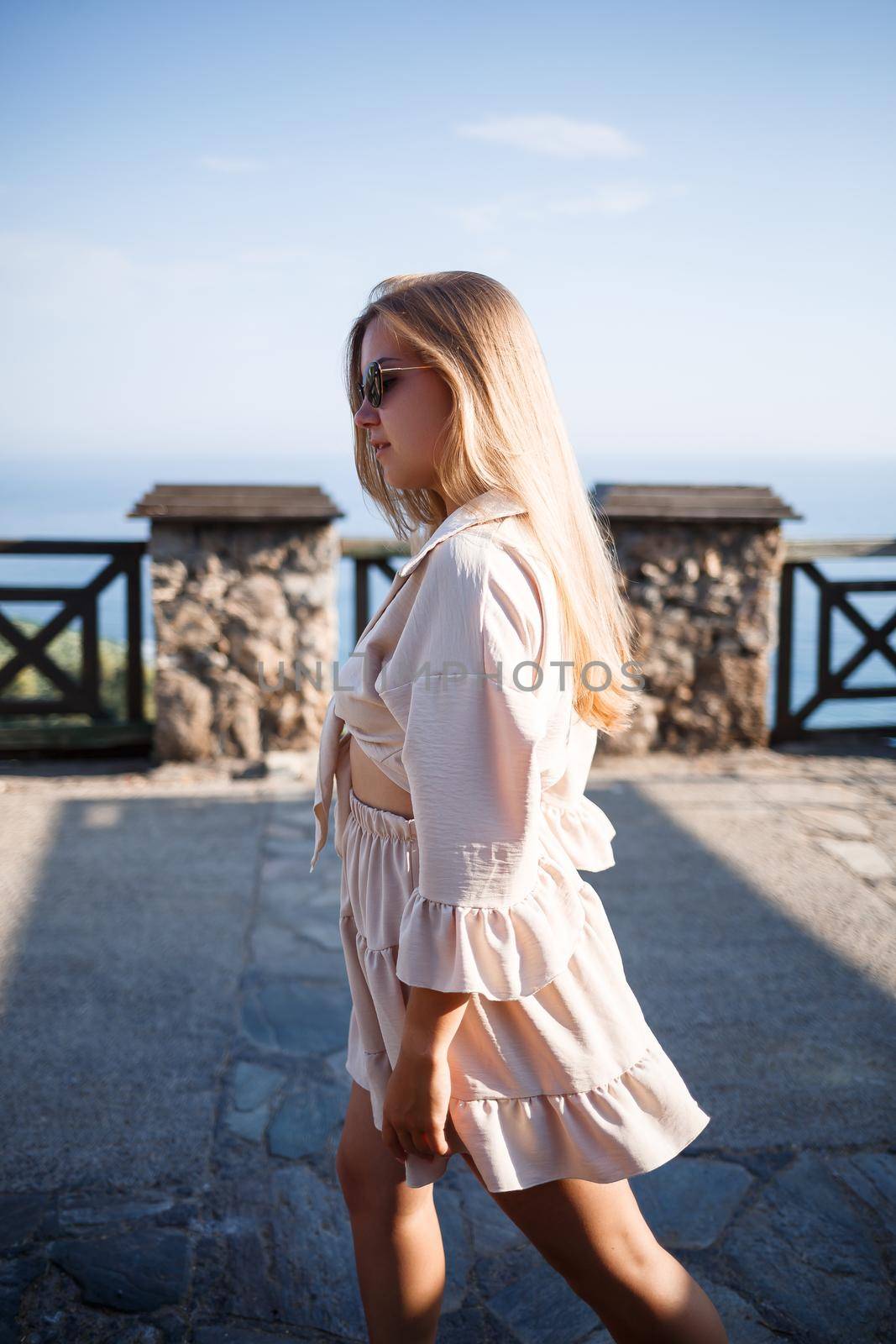 Young woman with long blond hair in a light top and skirt walks on a summer sunny day