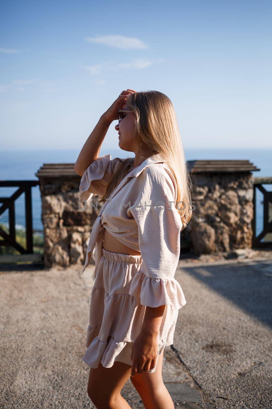 Young woman with long blond hair in a light top and skirt walks on a summer sunny day