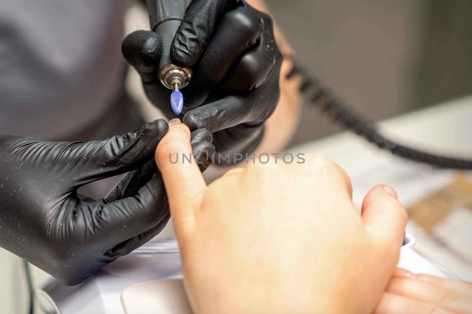 Manicure master uses electric nail file machine in a nail salon, close up. by okskukuruza