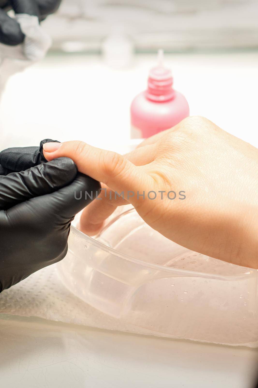 Close up professional manicure master holds the female hand of the customer and disinfects nails in a nail salon