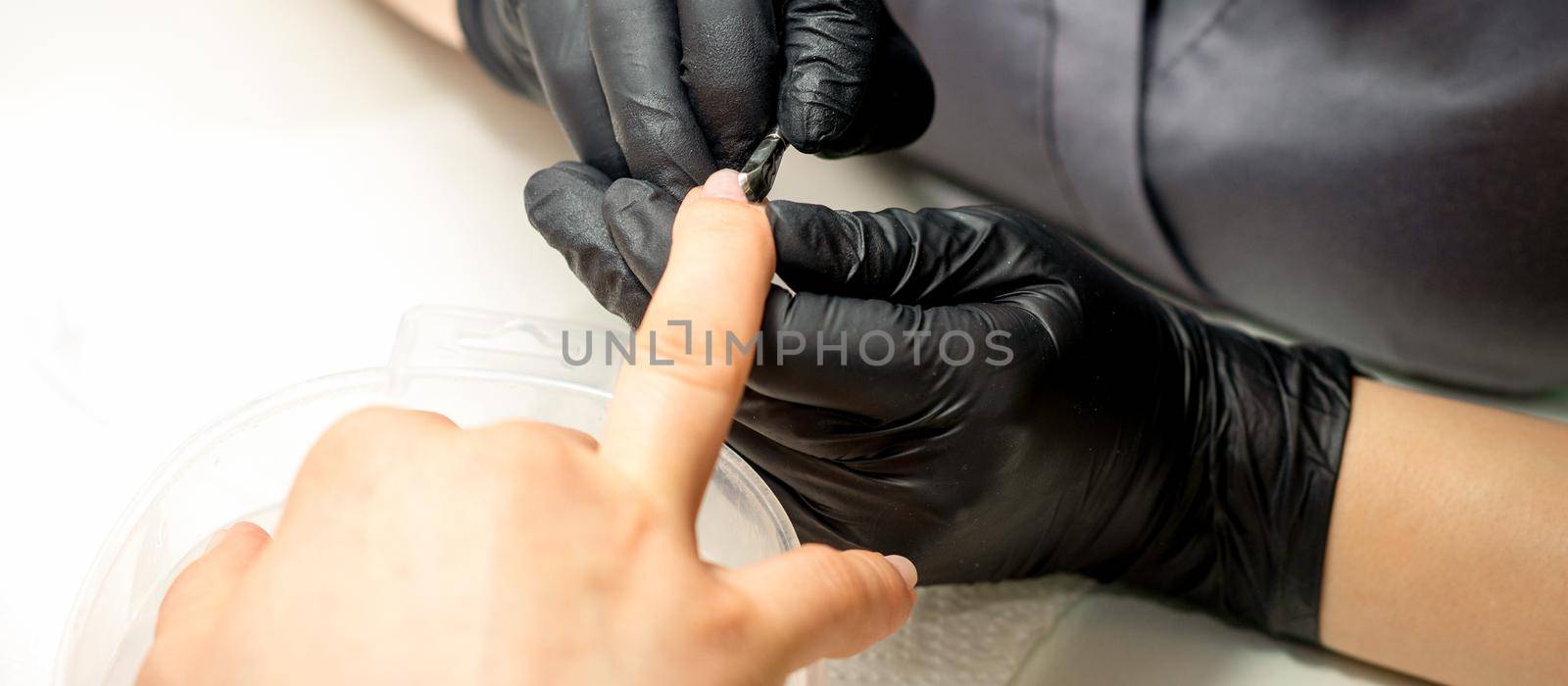 Close up professional manicurist master holding customer hand while using a cuticle pusher in a nail salon. by okskukuruza