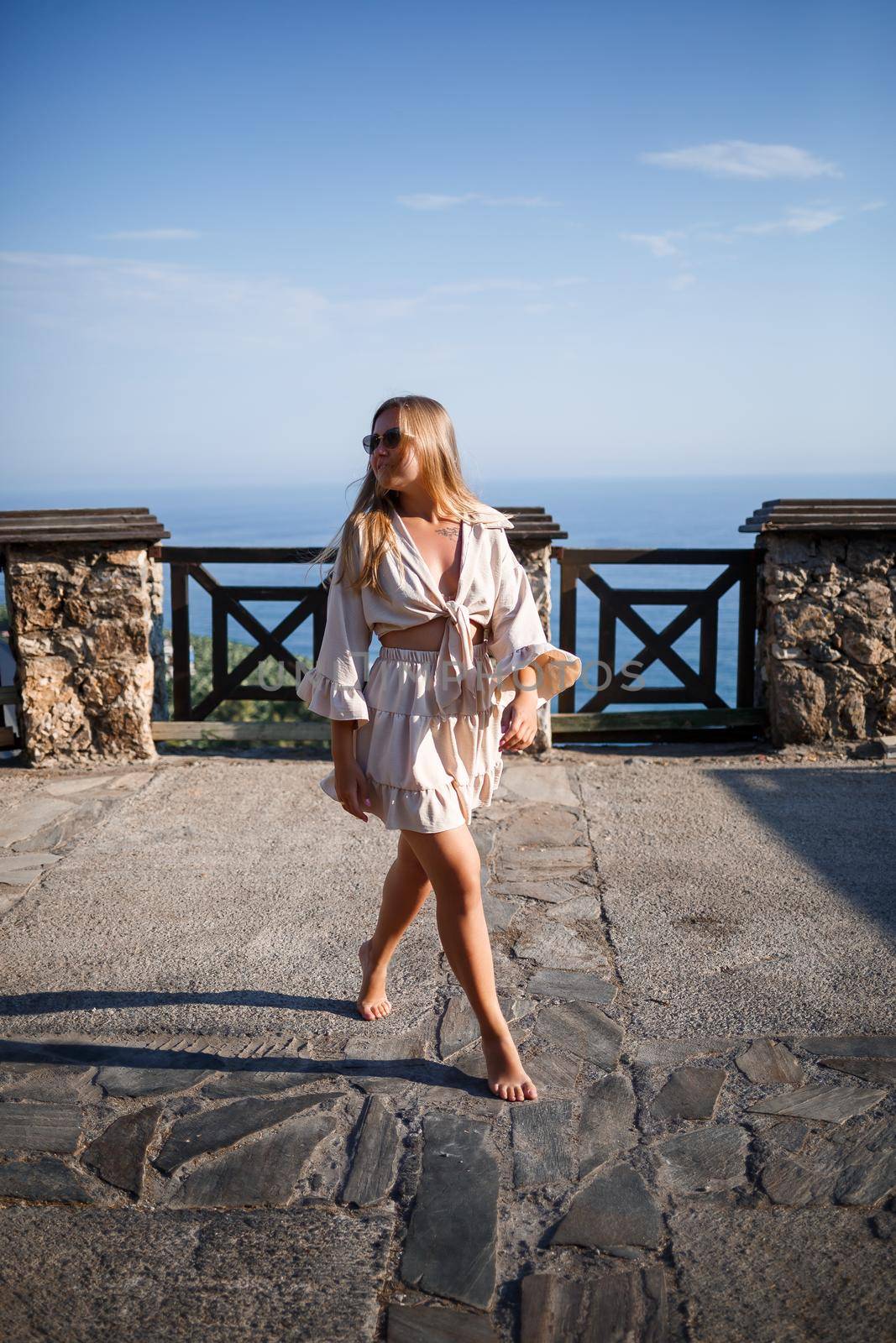 A young woman with long blond hair in a top and a skirt is walking on a summer sunny day. Happy girl with a smile on her face and in sunglasses is walking on a sunny day