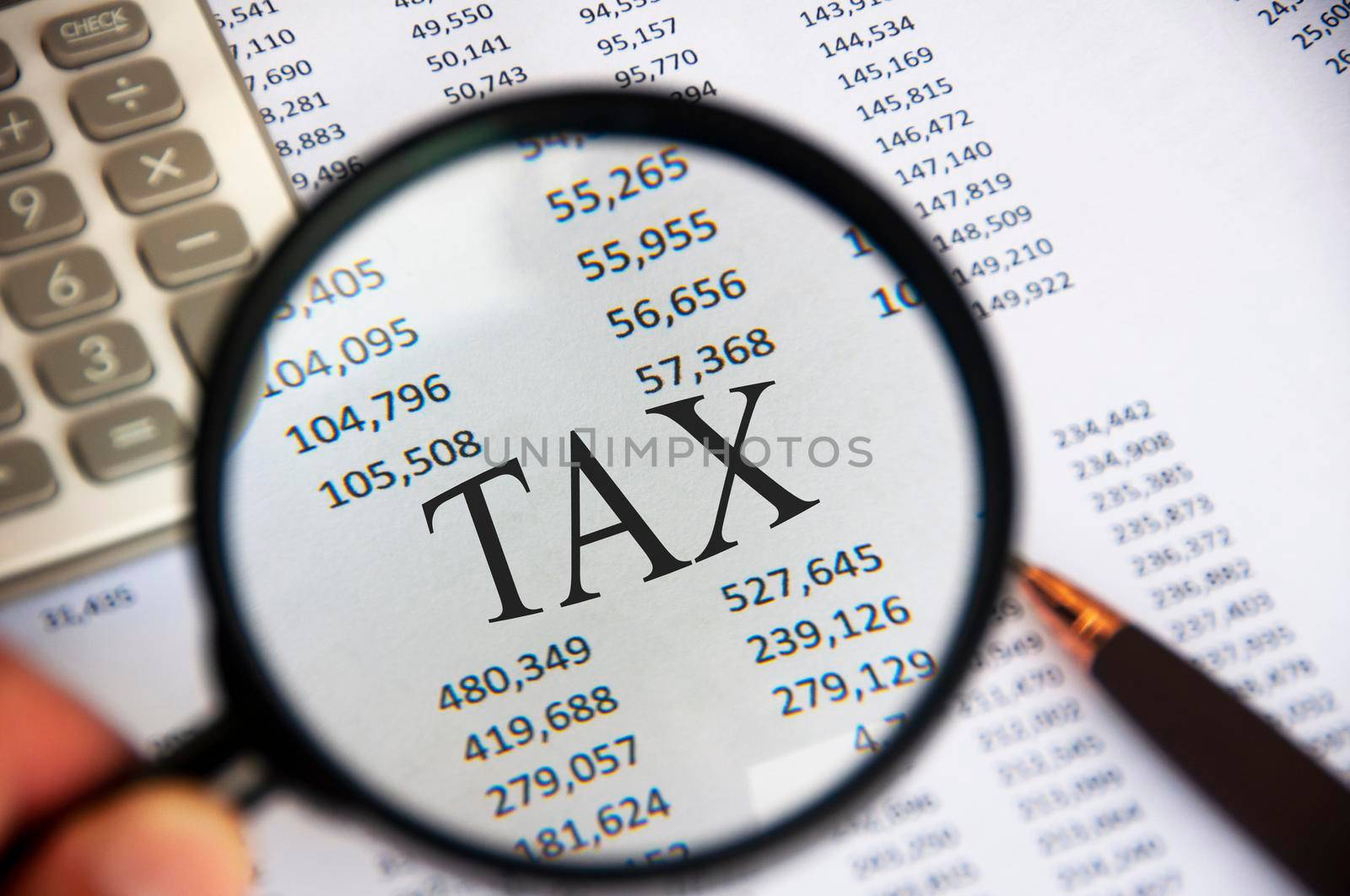 Magnifying glass focusing on TAX word on analysis paper. Tax concept.