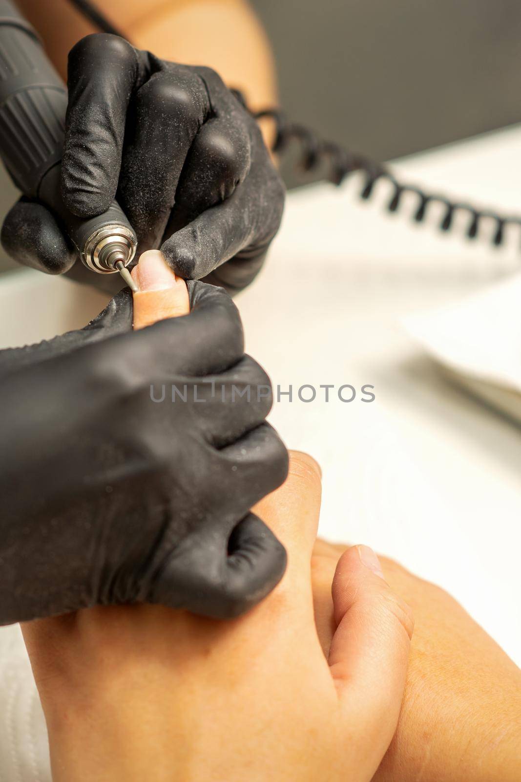 Manicure master uses electric nail file machine in a nail salon, close up