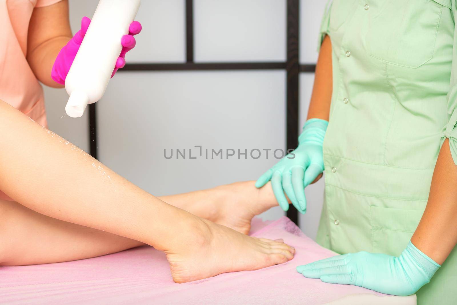 Procedure sugaring. A cosmetologist is sprinkling talcum powder on a young female leg before the depilation procedure. by okskukuruza