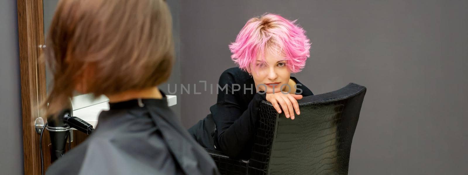 Portrait of a beautiful young caucasian woman with a new short pink hairstyle sitting in a chair at a hairdresser salon