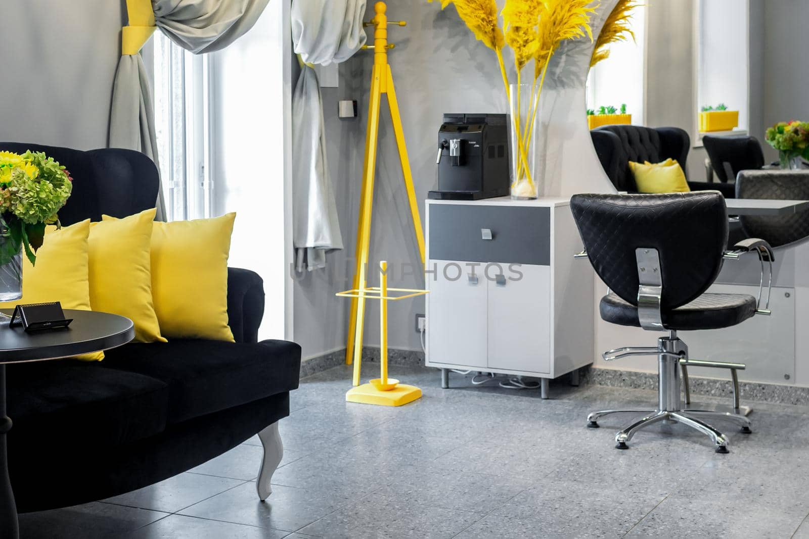 Modern small bright hair and beauty salon in black and yellow colors with gray walls and floor and black sofa with yellow cushions
