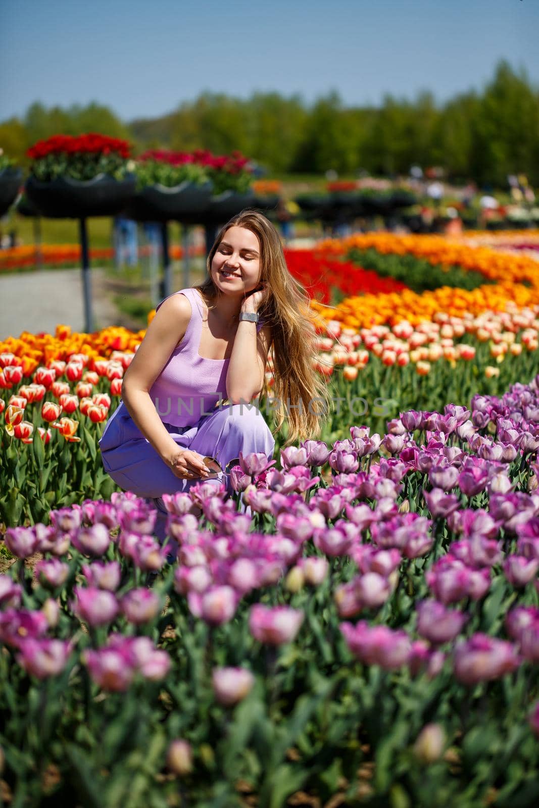 A young woman in a pink suit stands in a blooming field of tulips. Spring time