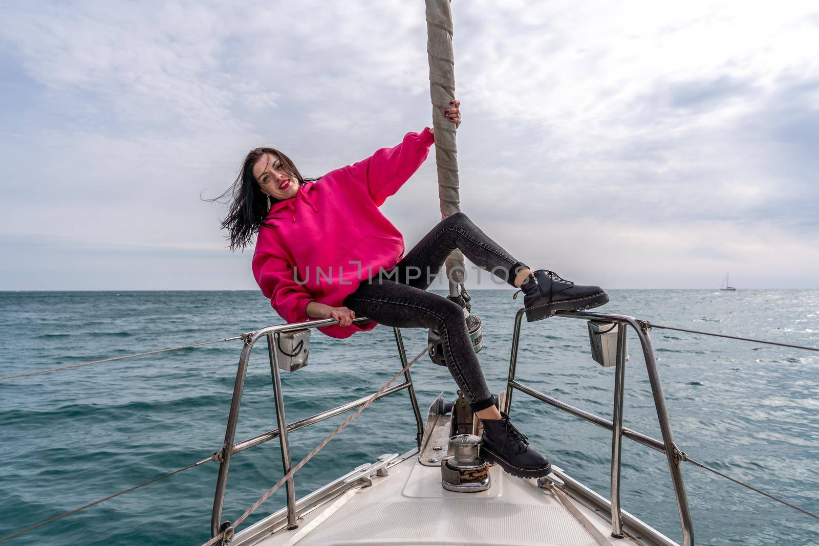 Woman standing on the nose of the yacht at a sunny summer day, breeze developing hair, beautiful sea on background by Matiunina