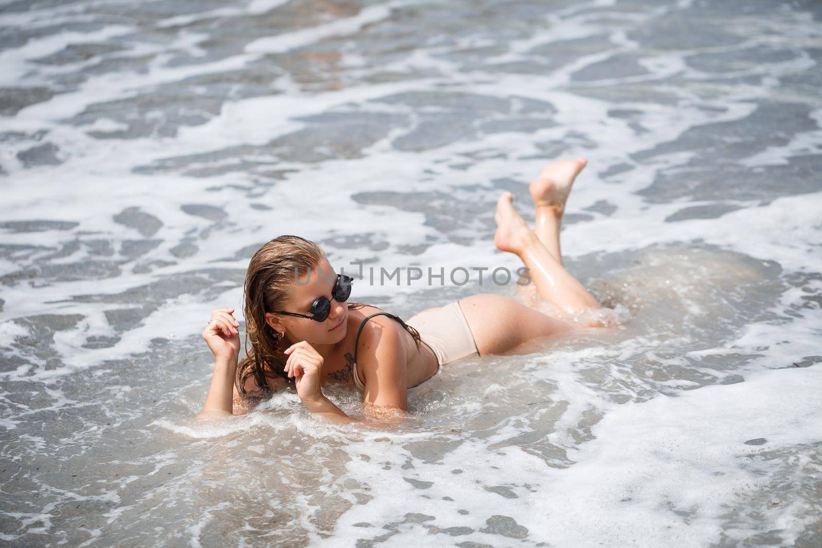 woman in beige swimsuit lies on an empty sandy beach near the ocean by Dmitrytph