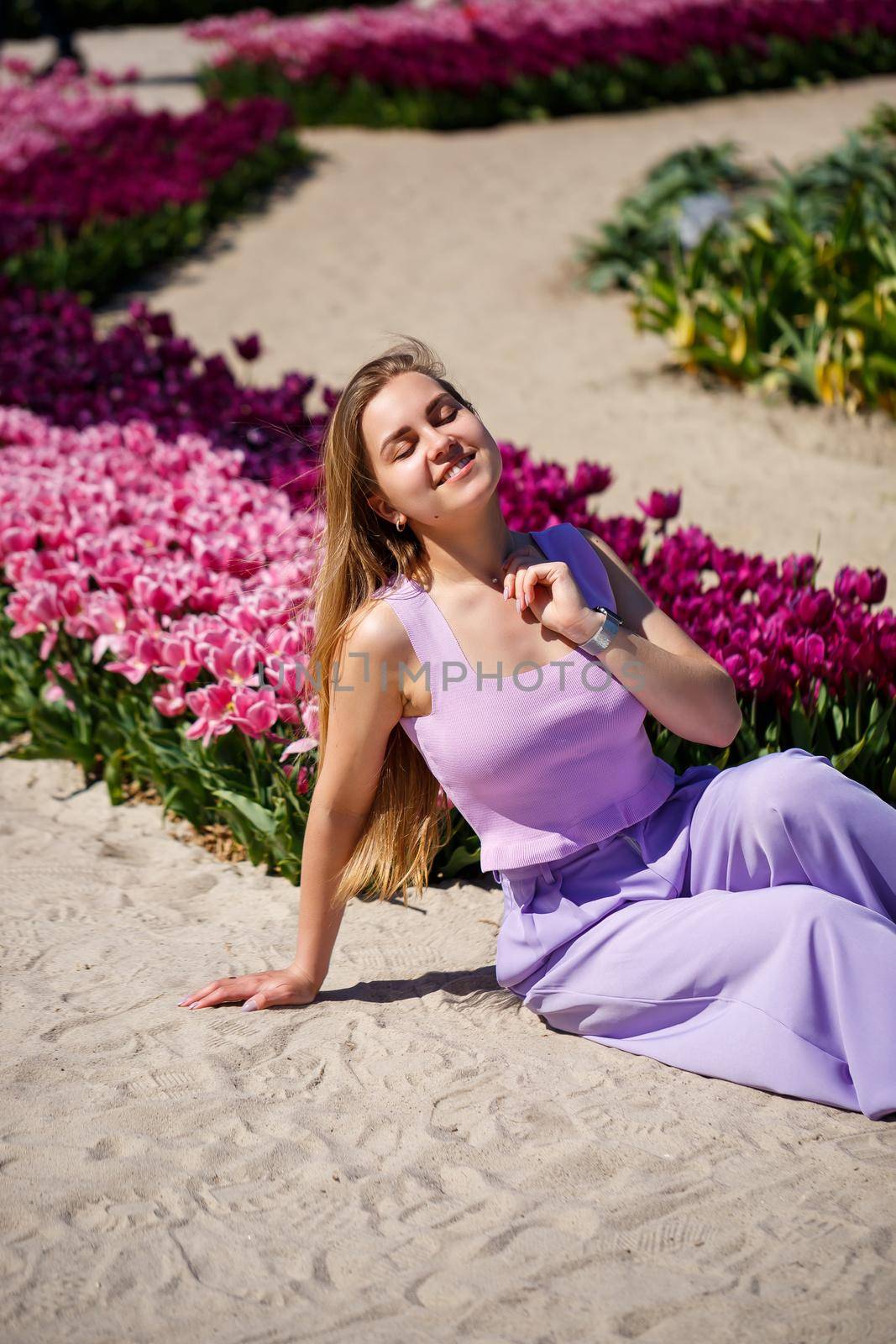 Back view of anonymous woman in summer dress and hat walking near blooming tulips in meadow on sunny day in nature by Dmitrytph