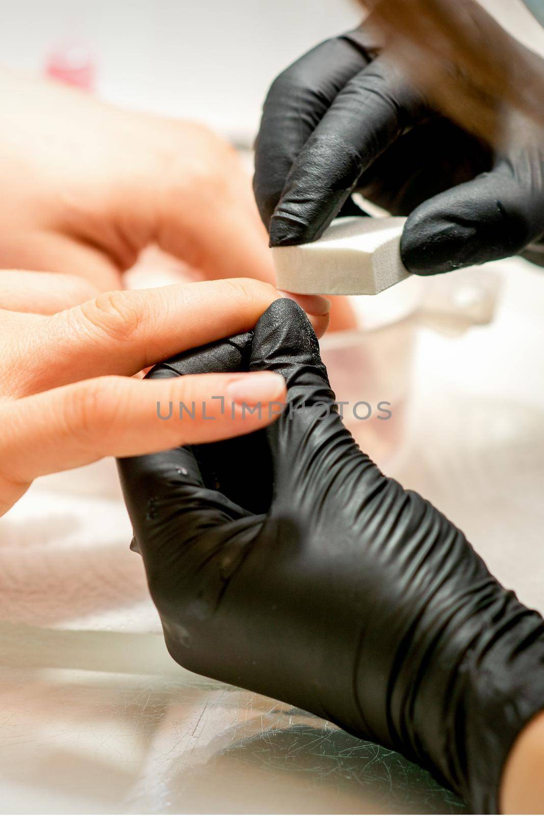 Close up of the caucasian hands of a professional manicurist are filing the nails of a young woman. Young caucasian woman receiving a manicure by a beautician with a nail file in a nail salon