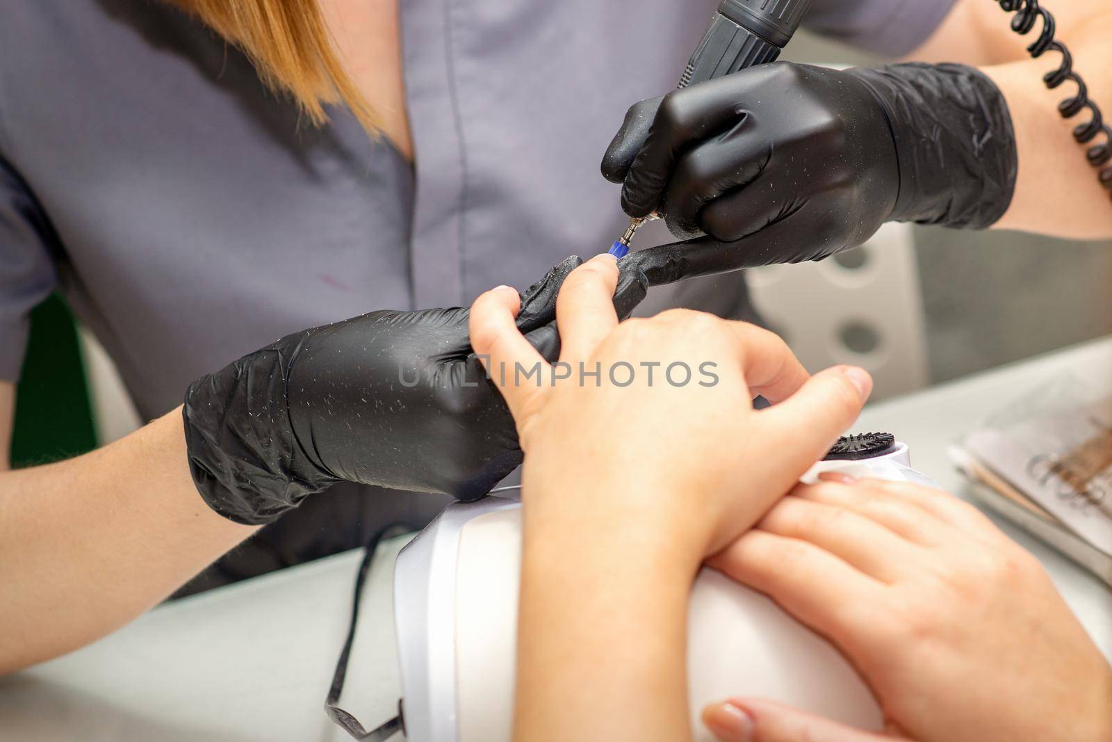 Manicure master in rubber gloves applies an electric nail file to remove the nail polish in a nail salon