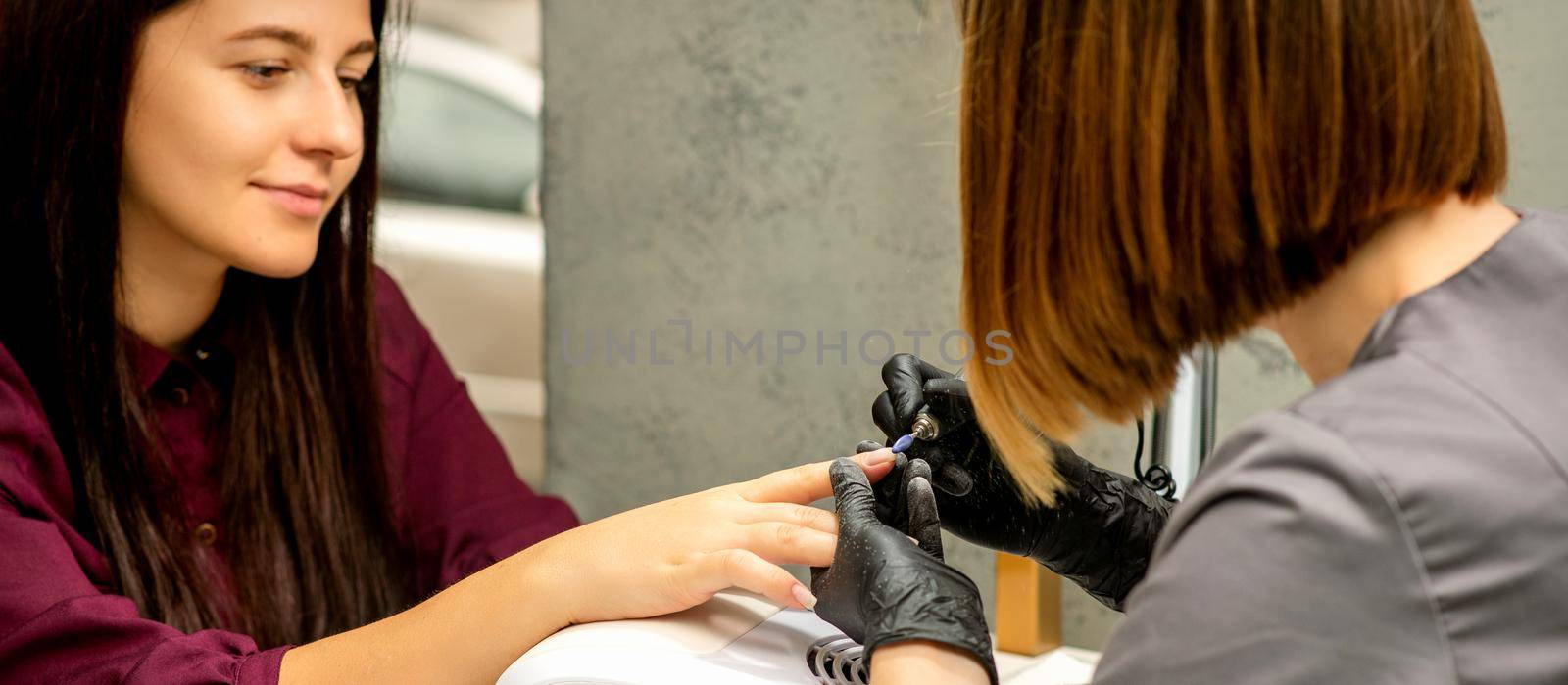 Manicure master in rubber gloves applies an electric nail file to remove the nail polish in a nail salon