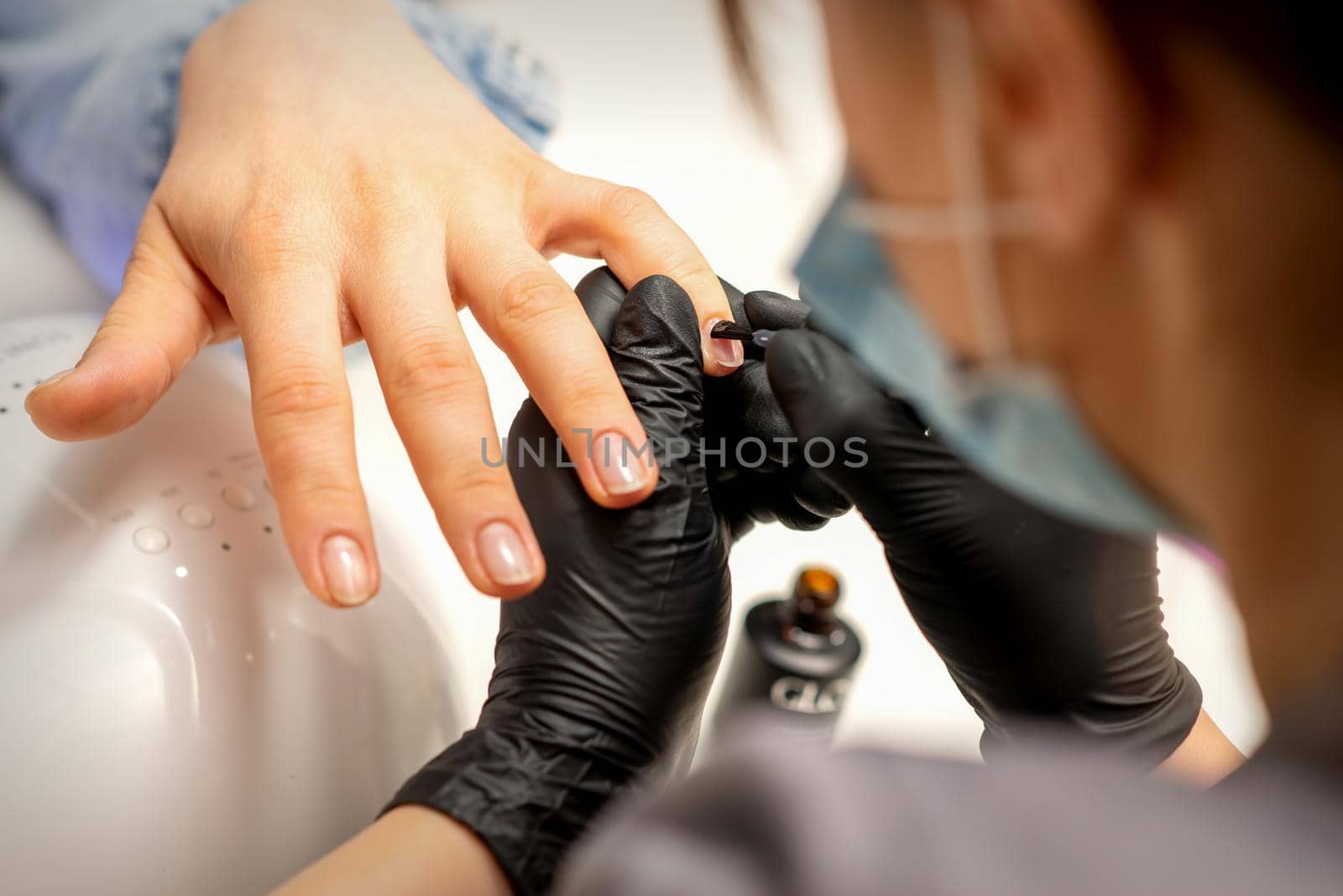 Manicure painting process. Manicure master paint the nails with transparent varnish in a nail salon, close up. by okskukuruza