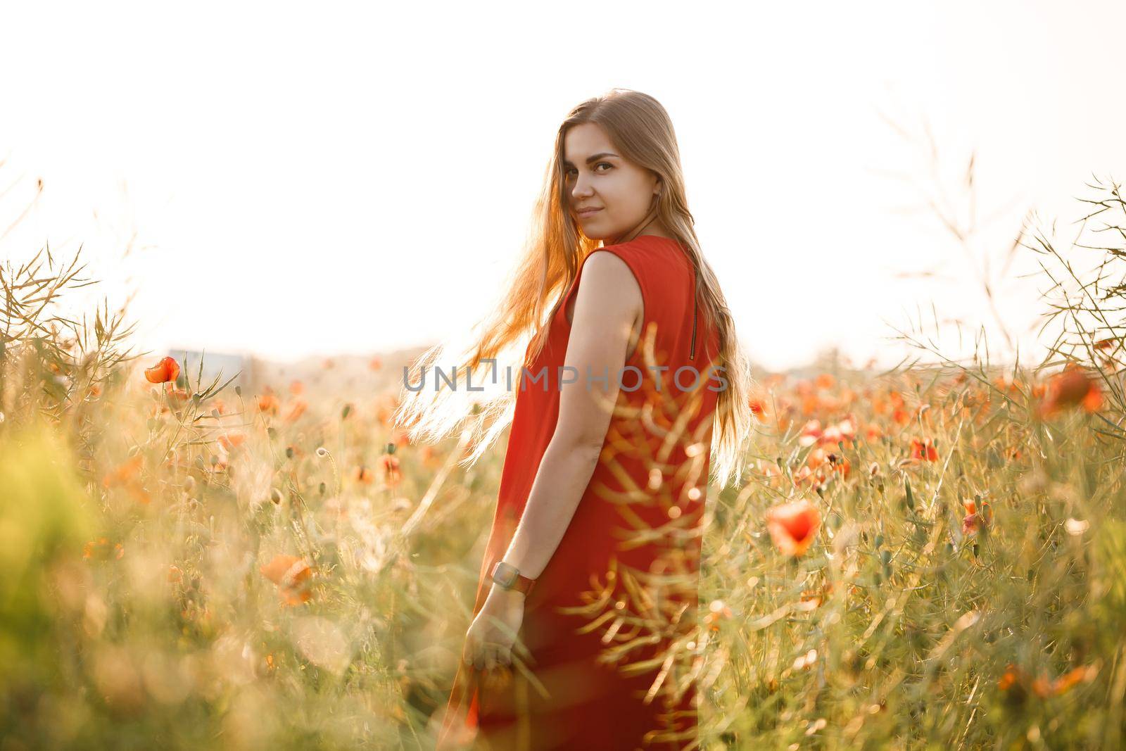Happy blonde woman in red dress holding a flower in her hair on a poppy field. Fun summer vibes. Relaxed atmosphere, positive emotions.