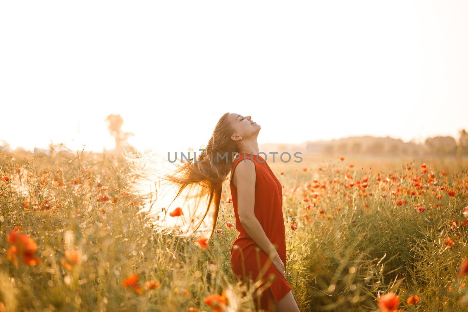 Beautiful woman in a red dress in a field of blooming poppies. Selective focus